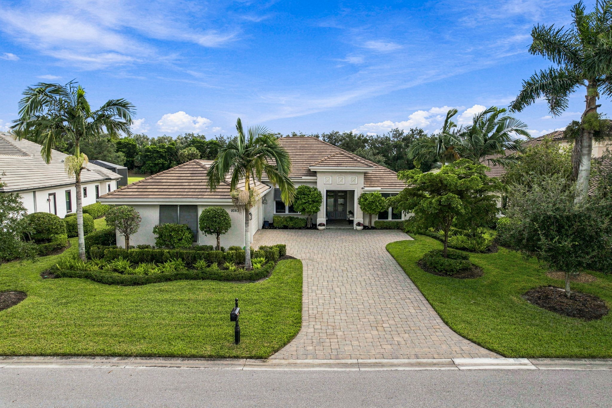 Sunlit luxury coastal home exterior in Florida with lush tropical landscaping and palm trees.